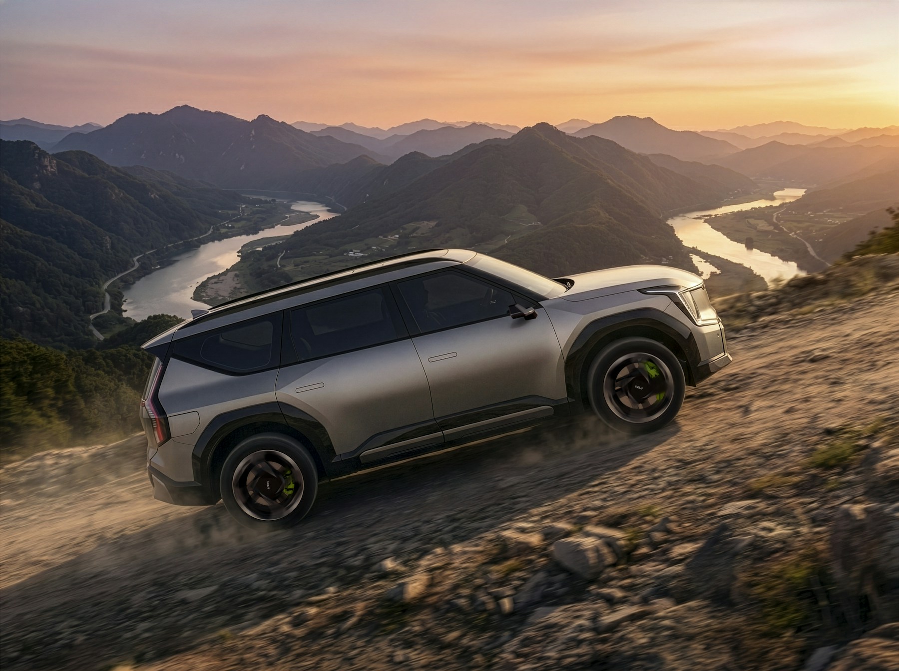 A large family SUV climbing a gravel mountain road above a river valley at sunset. Illustrative photography — not a vehicle held, offered for sale, or priced by Automotive Car Brokers.