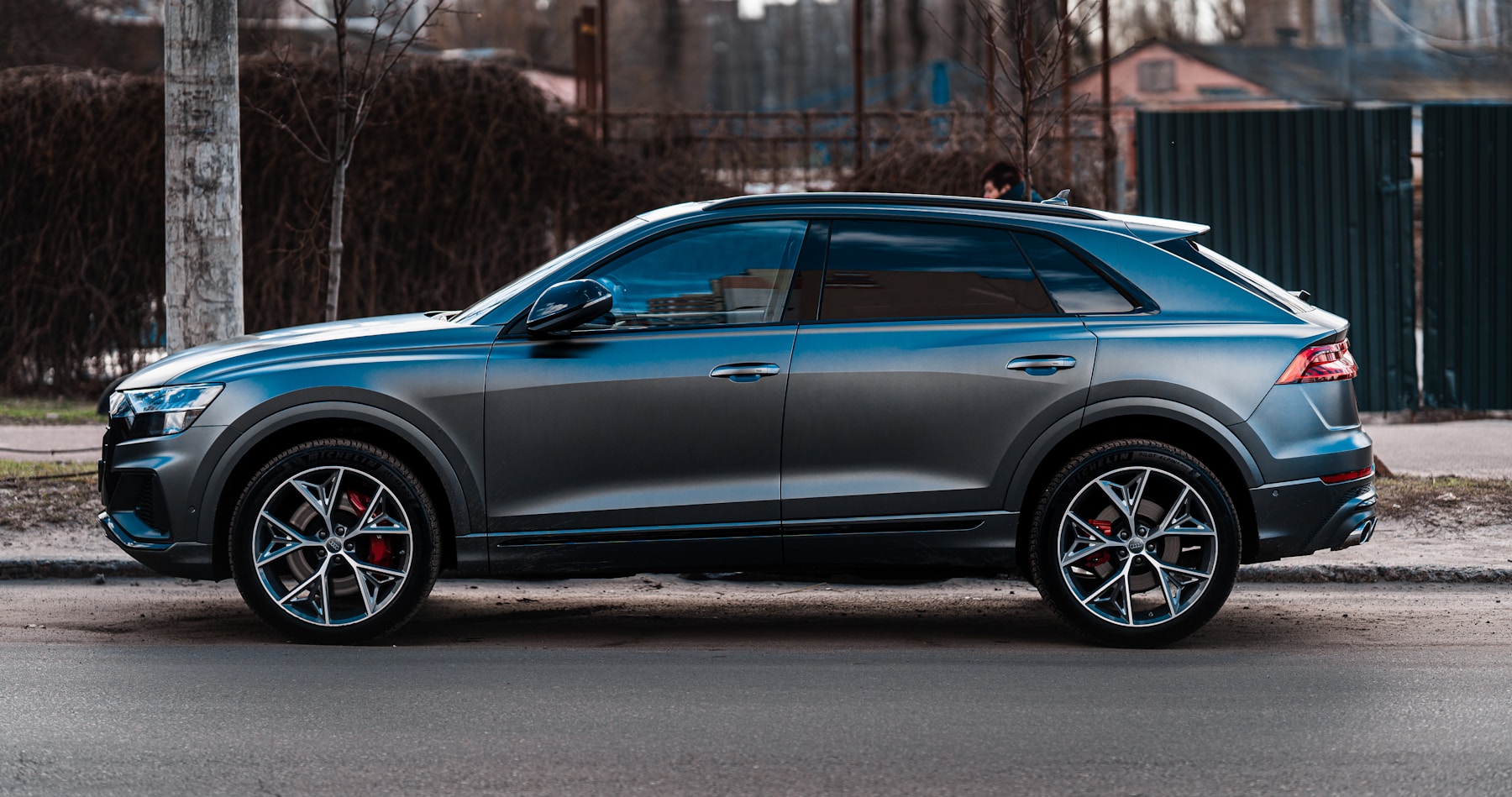 A dark gray crossover photographed side-on against a city hoarding. Illustrative photography — not a vehicle held, offered for sale, or priced by Automotive Car Brokers.