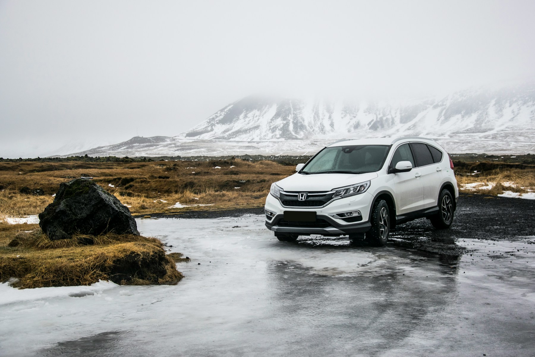 A white family crossover parked on wet ground in open country. Illustrative photography — not a vehicle held, offered for sale, or priced by Automotive Car Brokers.